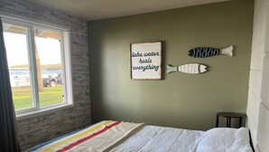 Une chambre avec un lit, une fenêtre, une citation encadrée au mur et un petit tabouret.