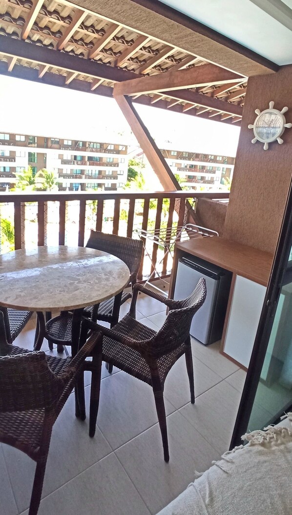 A balcony with a round table and wicker chairs, a small grill, and a clock on the wall. - Condominio Cupe Beach living Beira Mar (Ipojuca)