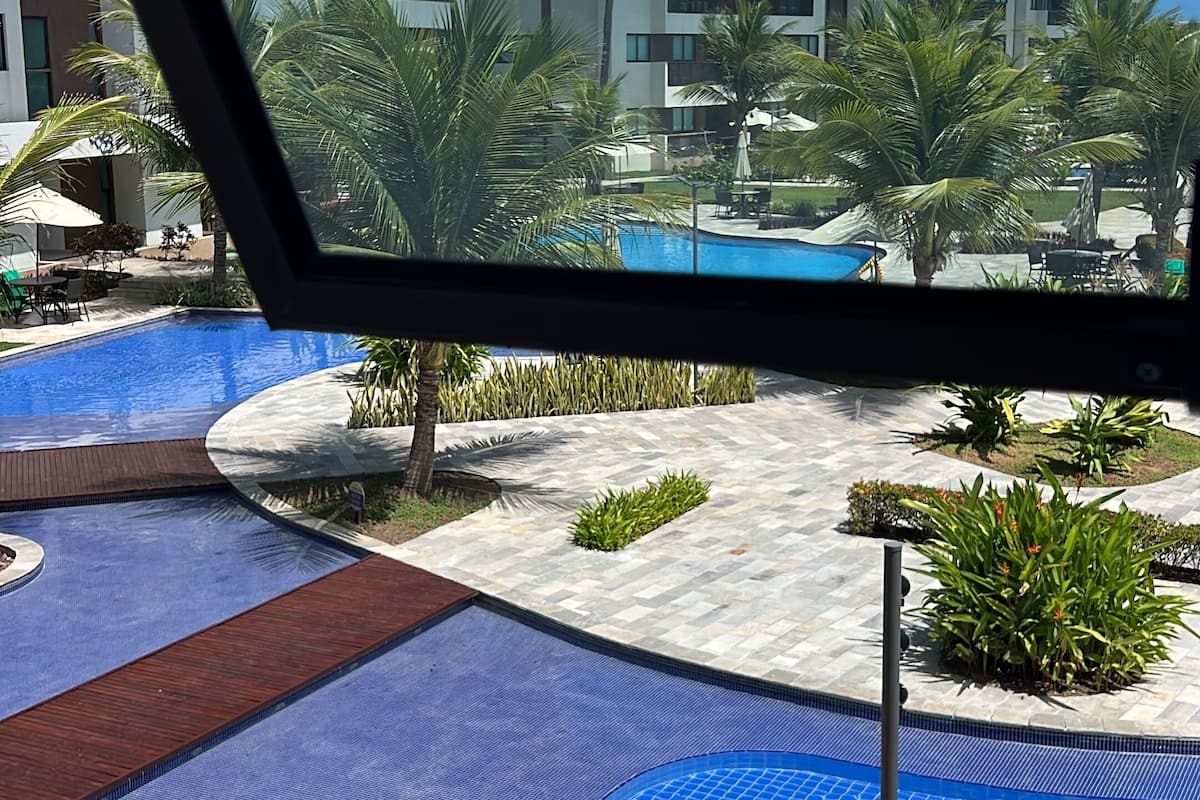 A pool area with a blue mosaic tile design, surrounded by palm trees and a building with balconies in the background.
