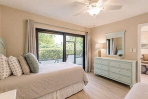 Ein Schlafzimmer mit einem Bett, einem Schminktisch, einem Deckenventilator und einem großen Fenster mit Vorhängen.