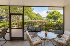Ein Balkon mit Glastür, einem runden Tisch, zwei Stühlen und einem Blumentopf.