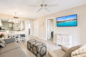 Ein modernes Wohnzimmer mit Essbereich, Deckenventilator und großem Fernseher an der Wand.
