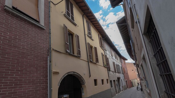 A narrow cobblestone street flanked by historic buildings with arched doorways and shuttered windows.