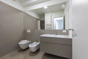 Un baño moderno con inodoro, bidé y un espejo grande.