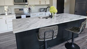 Una cocina moderna con una isla de mármol, taburetes de bar, electrodomésticos de acero inoxidable y un jarrón decorativo.