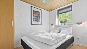 A bedroom with a bed, white brick walls, a wooden ceiling, a window with blinds, and a framed picture on the wall. - Lovely home in Glesborg with sauna (Glesborg)