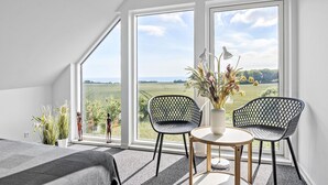 Une pièce avec une grande fenêtre, deux chaises, une petite table et un vase rempli de fleurs.