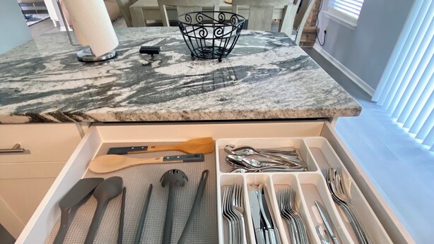 Una cocina con encimera de mármol, un organizador de cajones con utensilios y una zona de comedor al fondo.