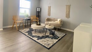 Una habitación amplia con un ventanal grande, un sofá color beige, una mesa de centro blanca y una alfombra estampada.