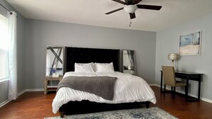 Un dormitorio con cama, ventilador de techo, escritorio, silla y alfombra.