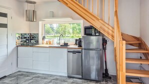 Una cocina moderna con escalera de madera, electrodomésticos de acero inoxidable y vistas a espacios verdes al exterior.
