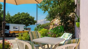 An outdoor seating area with a table and chairs, a parked van, and a scenic view of a body of water and mountains. - Amazing apartment in Stara Baska with WiFi (Stara Baska)