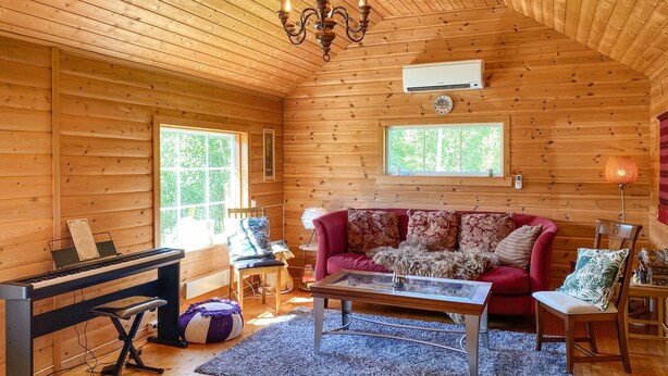 A cozy cabin interior with wooden walls, a piano, a red sofa, and a chandelier. - 2 bedroom pet friendly home in Haddal (Haddal)