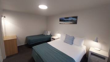 Ein Hotelzimmer mit einem Bett, einem Einzelbett, einem Nachttisch mit Lampe, einer Holzkommode und einem Bild an der Wand.