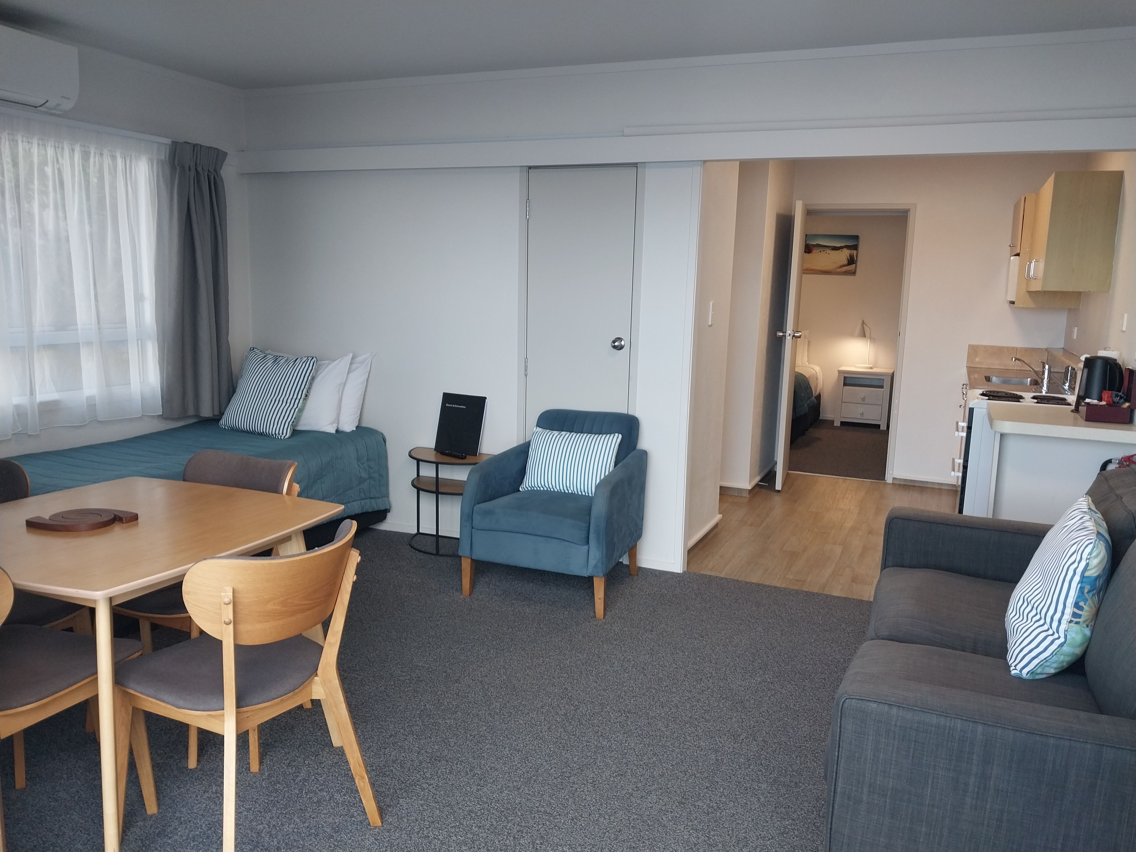 A compact hotel room with a bed, a desk, a chair, a sofa, and a kitchenette.