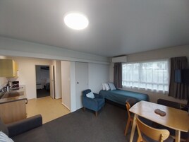 Una habitación compacta con cama, escritorio, silla, sofá y kitchenette.