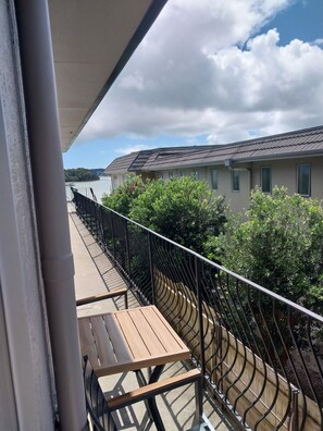 A balcony with a wooden table and metal railing overlooking a residential area with houses and a body of water. - Bayview Motel (Paihia)