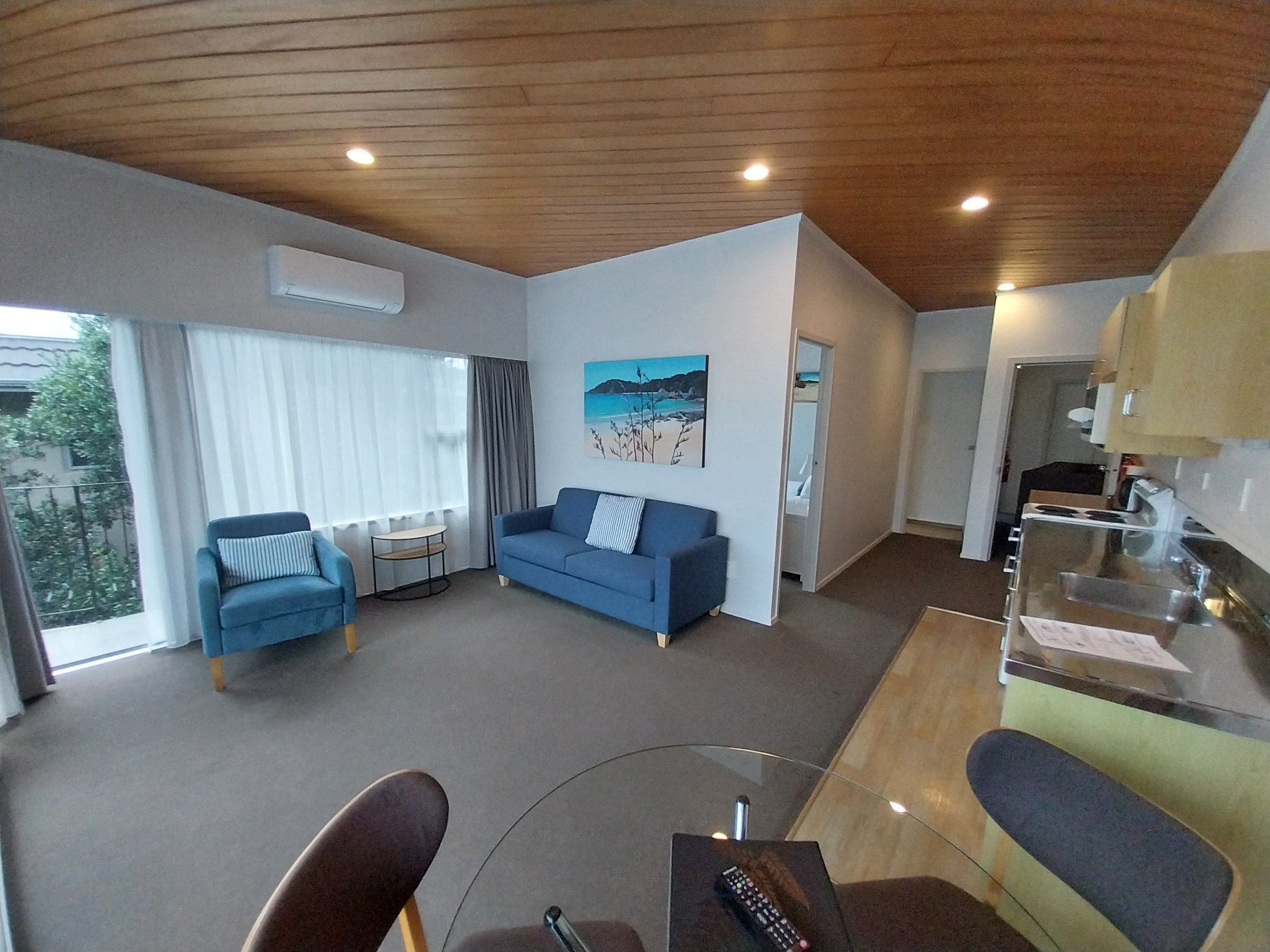 Uma sala de estar moderna com um sofá azul, uma poltrona, uma mesa de centro de vidro e um quadro na parede.