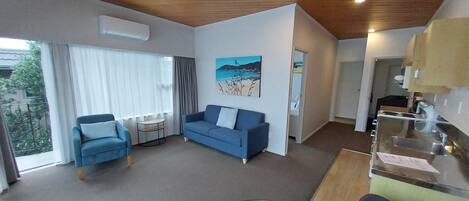 Uma sala de estar moderna com um sofá azul, uma poltrona, uma mesa de centro de vidro e um quadro na parede.