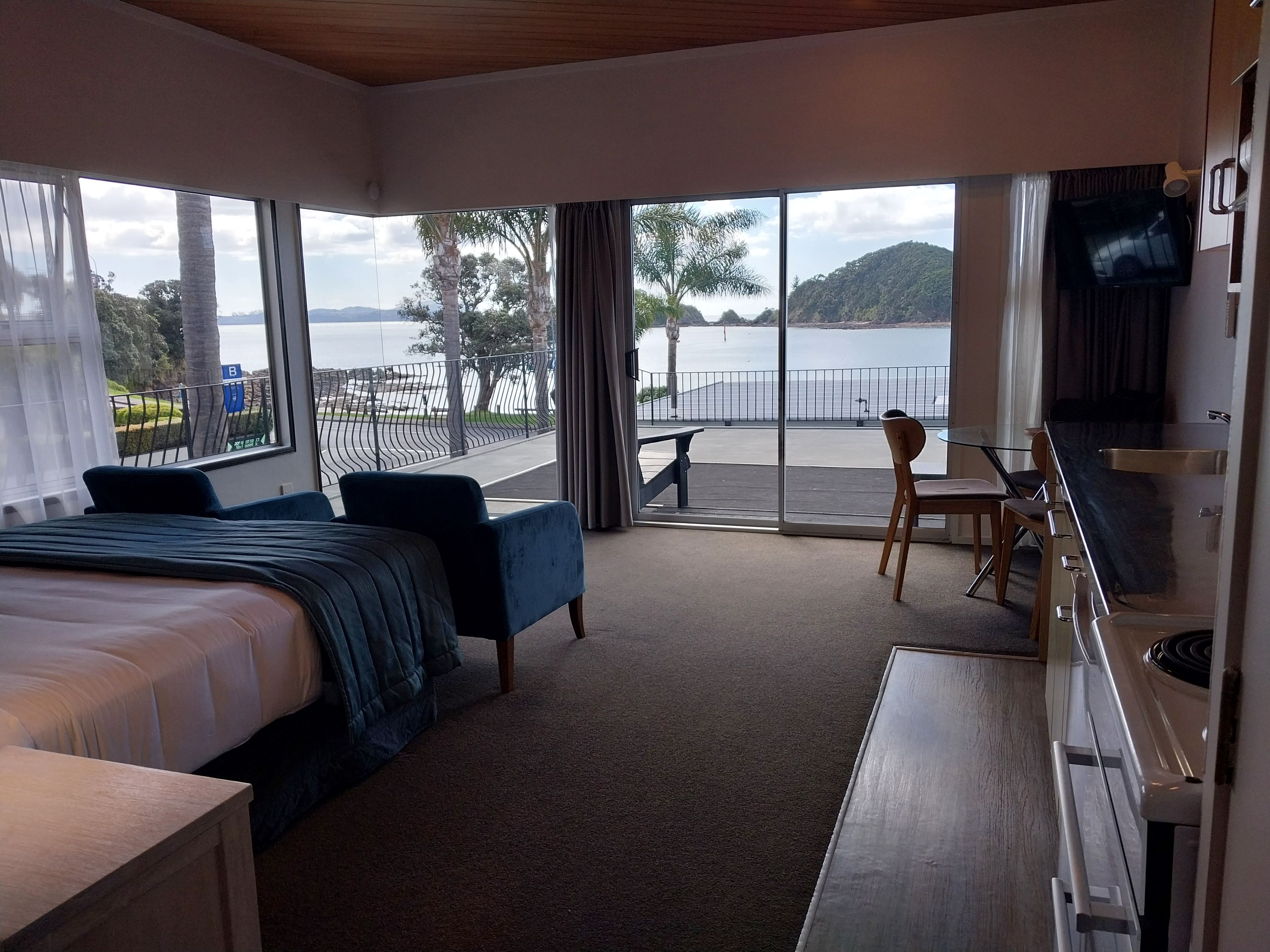 Une chambre d’hôtel comprenant un lit, un bureau, une chaise et un balcon avec vue sur la mer et les collines.