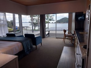 A hotel room with a bed, a desk, a chair, and a balcony with a view of the sea and hills. - Bayview Motel (Paihia)