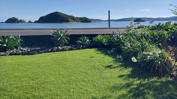 A grassy area with a view of a lake and distant islands. - Bayview Motel (Paihia)