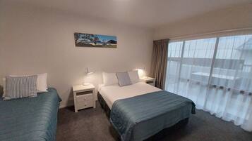 A hotel room with two single beds, a nightstand with a lamp, a painting on the wall, and a large window with curtains.