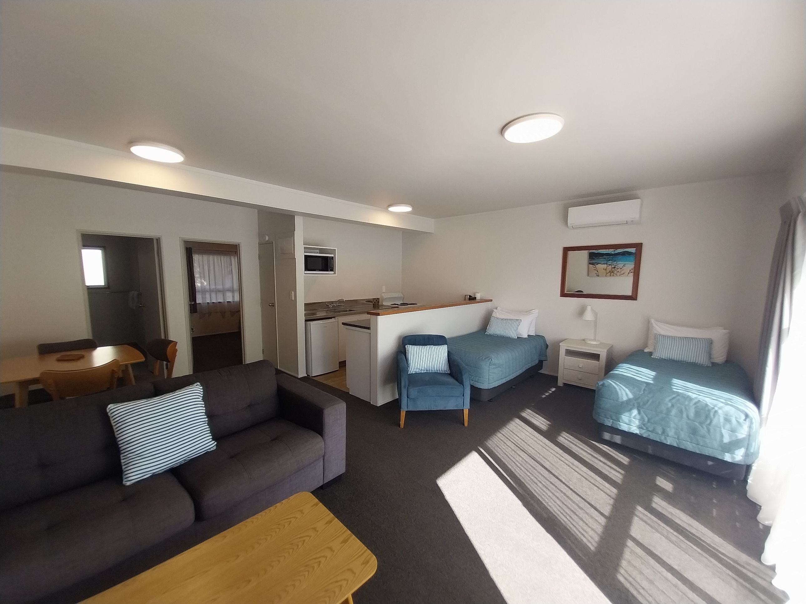 A compact hotel room with a kitchenette, a sofa, a bed, and a small dining area.