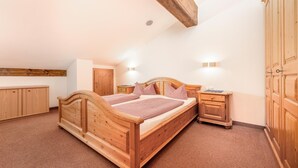 Een slaapkamer met een houten bed, nachtkastje, kledingkast en een plafond met zichtbare balken.