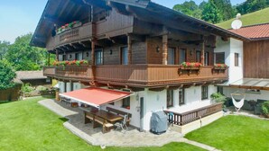 Een klassiek chalet met een houten balkon, terras buiten en een rood luifel.
