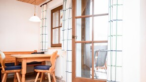 Een kamer met een houten eettafel en stoelen, een hanglamp en een groot raam met uitzicht.