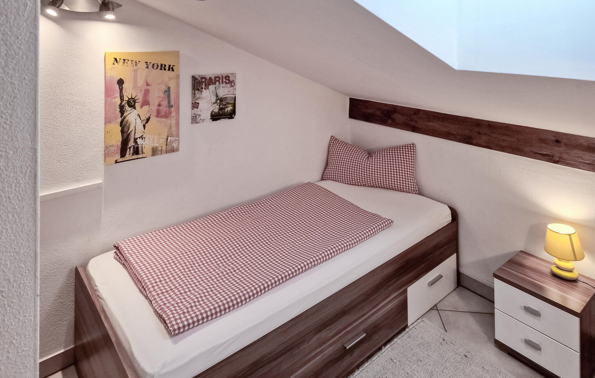 A single bed with a checkered bedspread, a nightstand with a lamp, and two posters on the wall.