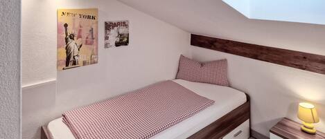 A single bed with a checkered bedspread, a nightstand with a lamp, and two posters on the wall.