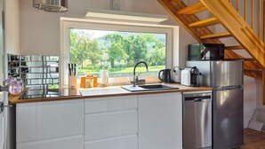 A modern kitchen with a stainless steel refrigerator, a built-in oven, and a microwave. There is a window providing a view of a green landscape.