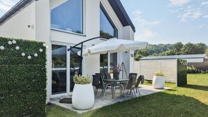 A modern house with a patio, large windows, and a dining area with outdoor furniture.