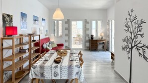 Un coin repas avec une table dressée pour quatre personnes, un canapé rouge et une bibliothèque.