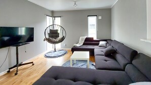 A modern living room with a large flat-screen TV, a hanging chair, a dark-colored sofa, and a white coffee table. - Lovely home in Perstorp (Perstorp)