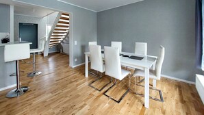 A modern kitchen with a white countertop and stainless steel appliances, a dining area with a white table and chairs, and a staircase leading to an upper level. - Lovely home in Perstorp (Perstorp)