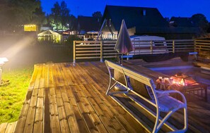En træterrasse med et bord, stole, bålsted og et telt.