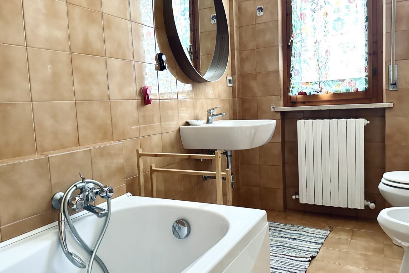 Un bagno con una vasca, un lavandino, uno specchio e una finestra con tende floreali.
