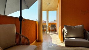 Un balcon ensoleillé avec deux fauteuils confortables, une table et un grand parasol.