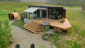 Una cabaña moderna con un porche de cristal, terraza de madera y un jacuzzi.