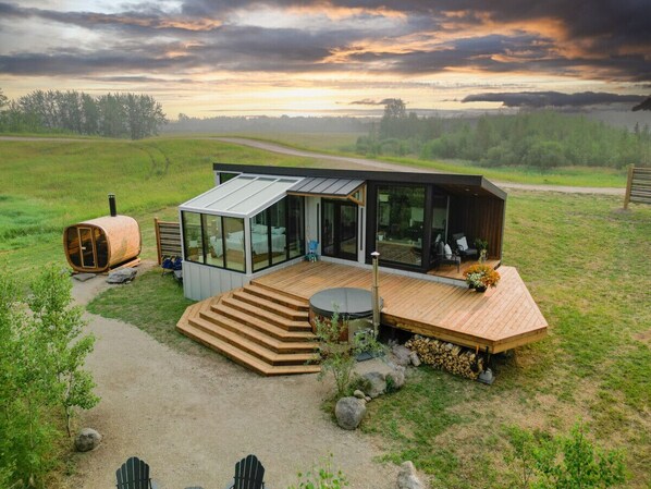 Eine moderne Hütte mit Glaserker, Holzterrasse und Whirlpool.