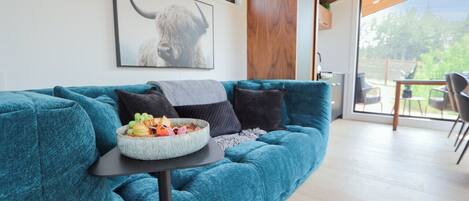 En tealfarvet sofa med en skål frugt og et tæppe, et rammet dyrebillede og et træskab.