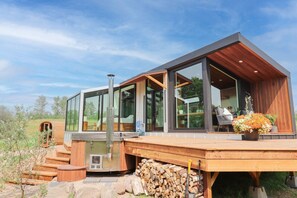Ein modernes Haus mit großen Glasfenstern, einer Holzterrasse und einer Sauna.