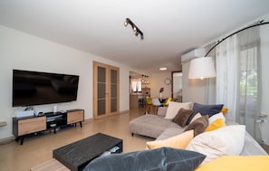 Ein modernes Wohnzimmer mit Fernseher, einer Couch, einem Couchtisch und einem Essbereich im Hintergrund.