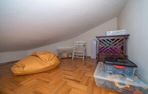 Ein Zimmer mit Holzdielen im Fischgrätmuster, einem Sitzsack, einer weißen Leiter, einem Kunststoff-Aufbewahrungsfach und einem Holzschrank mit violettem Gittermuster.
