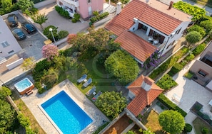 An aerial view of a residential area with a swimming pool, a tennis court, and a house with a red-tiled roof. - Nice home in Kozino with sauna (Kozino)