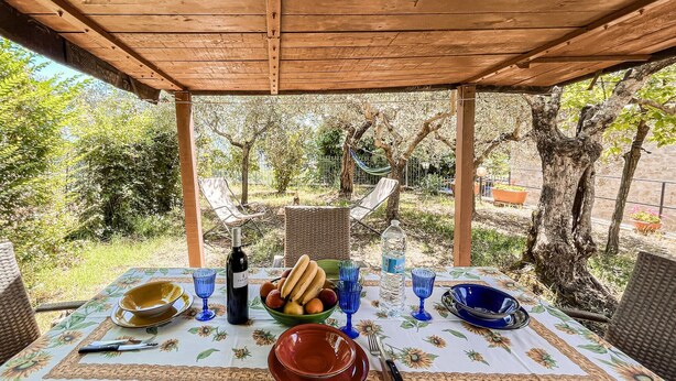 An outdoor dining area with a table set for two, featuring a bottle of wine, a bowl of fruit, and blue glassware. - 2 bedroom pet friendly home in Todi (Todi)