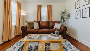 A living room with a brown leather sofa, a coffee table with magazines, a floor lamp, and a large window with curtains. - Historic Revival King Bed Liberty Bowl Memphis 895 (Memphis)